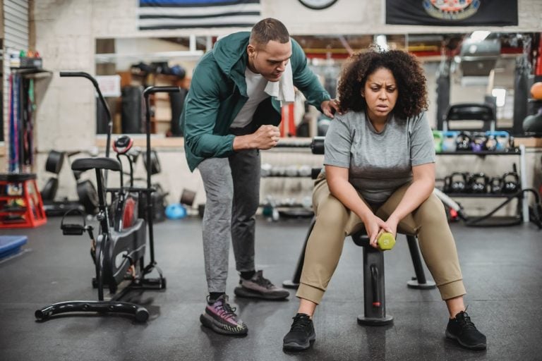 personal male trainer with overweight female client in fitness center