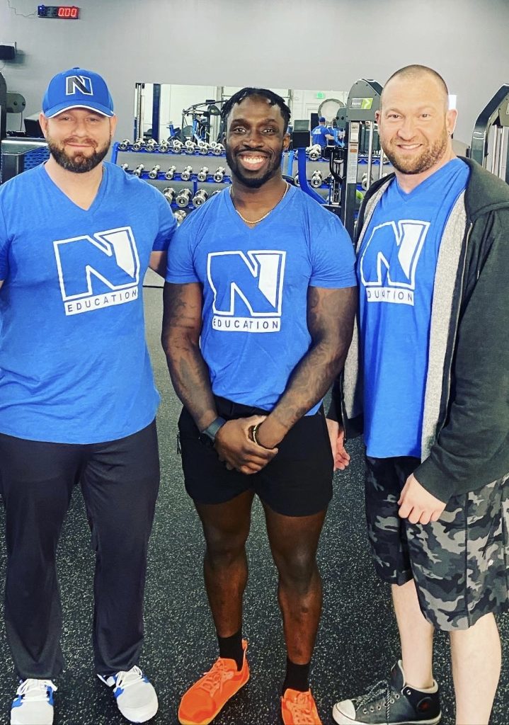 Owner of Fitness Factory KC attending an out-of-state practical course, actively participating in a hands-on training session, surrounded by fitness professionals and gym equipment, enhancing skills and knowledge to bring back to the gym.