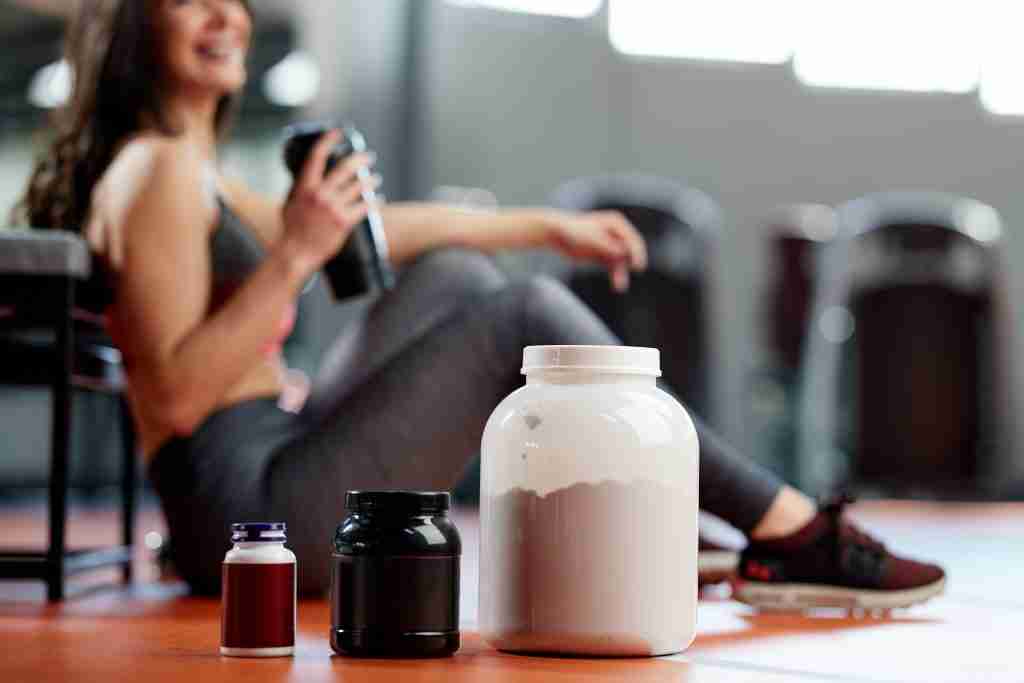 protein, amino acid, and multivitamin supplements in front of seated woman