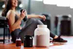 protein, amino acid, and multivitamin supplements in front of seated woman