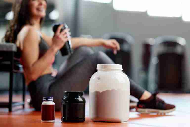 protein, amino acid, and multivitamin supplements in front of seated woman