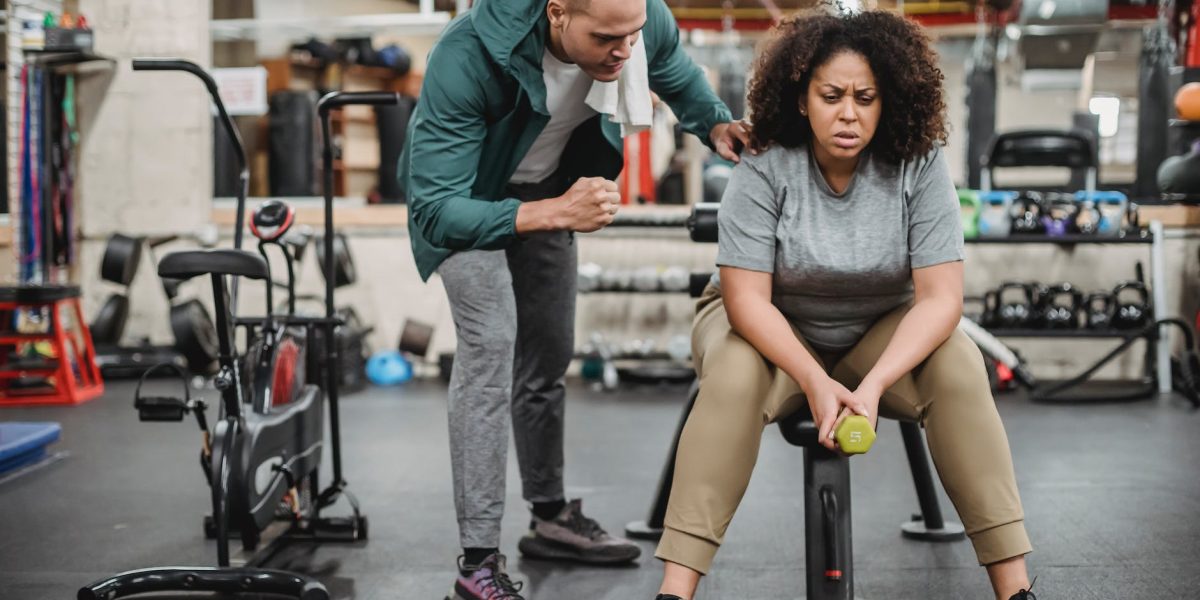 personal male trainer with overweight female client in fitness center