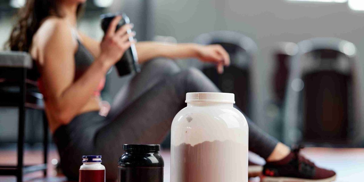 protein, amino acid, and multivitamin supplements in front of seated woman